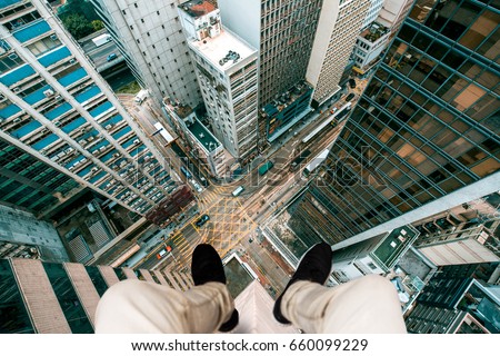 Extreme photography concept, Man sitting at the edge of a building taking photo