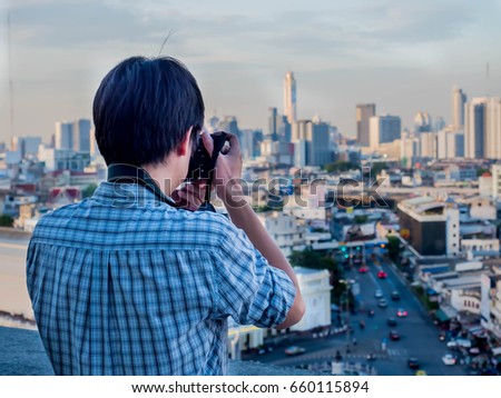Young man shooting outdoor photos  take a picture of the city on a tall building.