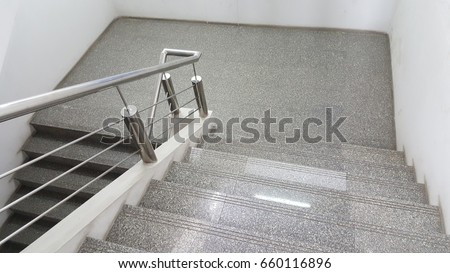 The stairs at work are covered with marble tiles and railing against made of stainless steel. Reflector from jar lamp on ceiling. Royalty-Free Stock Photo #660116896