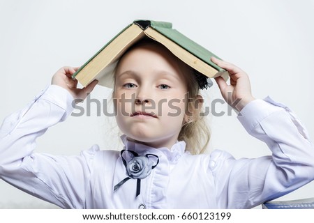 Pretty curly little girl standing and holding book above her head over white background