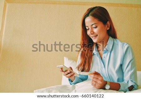 Beautiful Asian woman take a rest on bed and using smart phone