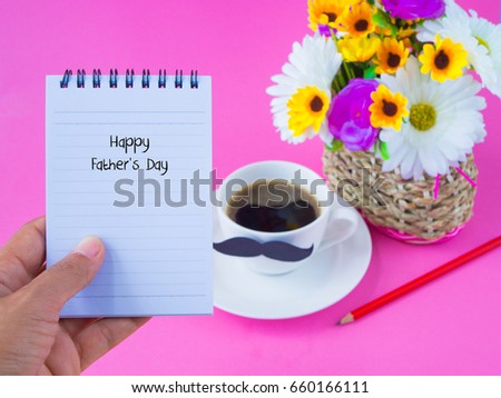 Father's day concept. Hand holding not book with Happy Father's Day message on note book with pink flower, coffee cup with black Mustache on pink background