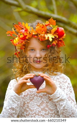 A child dressed as a fairy stands
in an autumn forest.She holds a purple heart in her hands.
She poses for the camera holding up the sign of love for
all to see.
