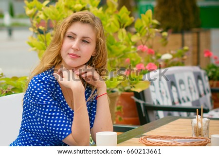 Cute European girl sitting in a cafe drinking coffee and waiting for a friend. A young woman in a summer terrace smiling and having fun