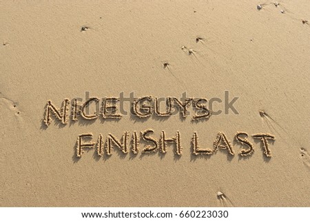 Handwriting  words "NICE GUYS FINISH LAST" on sand of beach. Royalty-Free Stock Photo #660223030