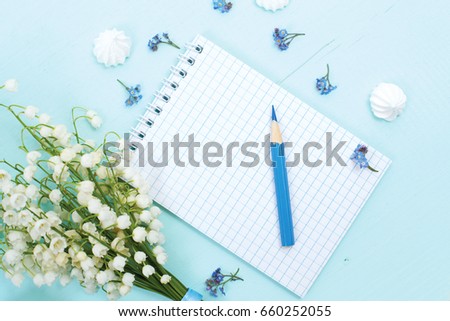 A bouquet of lilies of the valley, a notepad and a pencil lie on a blue wooden table