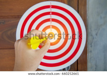 Close up of hand of businessman holding the arrow with number and dart at the target business.
