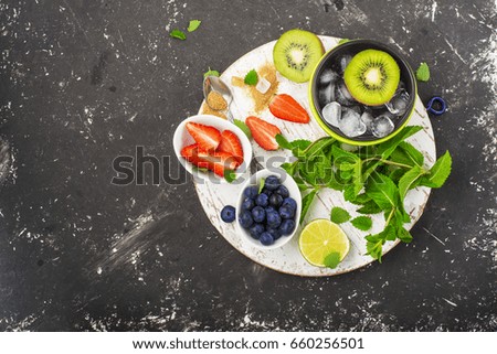 Bright juicy ripe berries and fruits for summer healthy recipes, cooling drinks, breakfasts, snacks in lunch boxes: kiwi, strawberries, cherries, blueberries,  Top view on a dark background.
