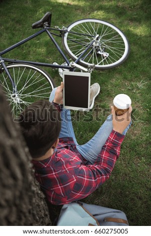 Overhead view of man using digital tablet and drinking coffee on green lawn