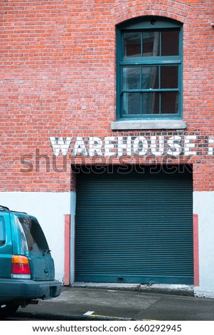 Corrugated gate in a brick building several floors with an old window and an inscription warehouse on the surface of a brick wall