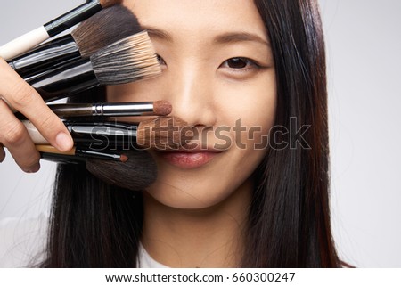 Beautiful asian woman holding a cometic brush portrait on a gray background.