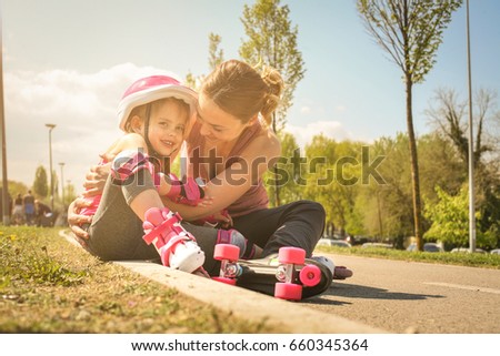Smiling mother with her little daughter sitting on road after skating.