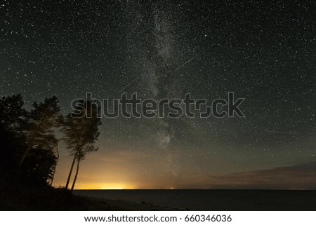 Milky way galaxy stars light over the coast of the sea water with forest trees and city lights in summer night