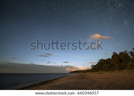 Milky way galaxy stars light over the coast of the sea water with forest trees and city lights in summer night