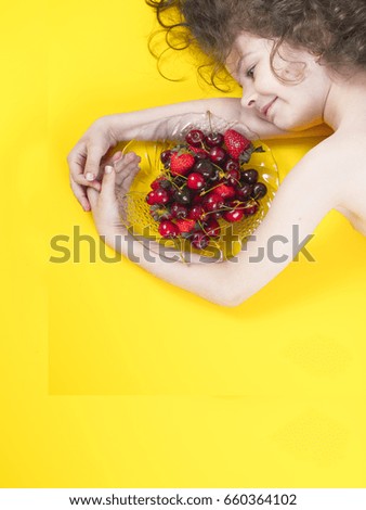 Portrait of cute smiling boy lies on a yellow background with plate of fruit