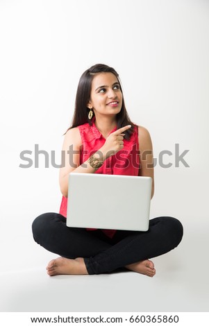 Attractive Indian/Asian girl in casual wear using laptop computer while sitting isolated over white floor