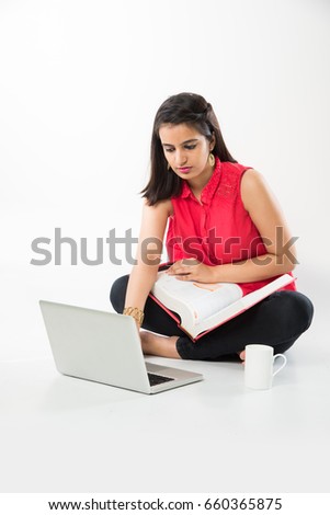 Attractive Indian/Asian girl student studying on laptop computer with pile of books, sitting isolated over white floor