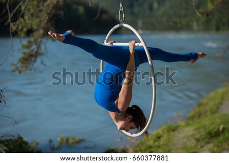 red-haired gymnast in a blue suit doing the difficult exercises at the air ring in nature