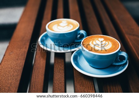 Two cups of cappuccino with latte art on wooden background. Beautiful foam, greenery ceramic cups, diagonal composition, place for text. Royalty-Free Stock Photo #660398446