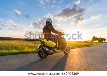 Motor biker riding on empty road with sunset light, concept of speed and touring in nature. Small motorcycle scooter Royalty-Free Stock Photo #660404869