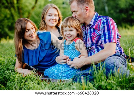 Ideal picture of family happiness - happy family with two daughter having fun and lying on the grass on a summer day in sunset. Parenthood, love, vacation and happy family concept.