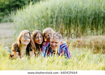 Ideal picture of family happiness - happy family with two daughter having fun and lying on the grass in lake shore on a summer day in sunset. Parenthood, love, vacation and happy family concept.