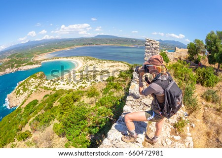 Travel woman photographer takes shot of Voidokilia Beach from famous Navarino Castle ruins in Pylos, Peloponnese, Greece after hiking.Hiker woman photographing on fortress walls. Scenic fish eye view.