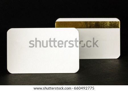 A photo of two blank white business cards with rounded corners, one of them with a golden stripe, on a black background, with a place for text