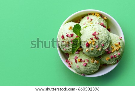 Bowl of green pistachio ice cream and dried fruit pieces isolated on green background. Top view