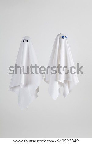 Couple of white sheet ghost with doll's eyes isolated on a white background. Minimal pop still life photography and tones on tones