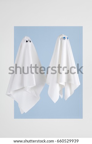 Couple of white sheet ghost with doll's eyes isolated on a white background white blue frame. Minimal pop still life photography