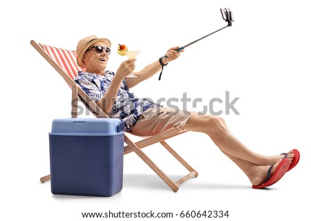 Happy elderly tourist with a cocktail sitting in a sun lounger and taking a selfie isolated on white background