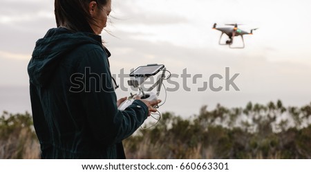 Young woman navigating a flying drone with remote control. Woman in countryside flying drone and taking pictures. Royalty-Free Stock Photo #660663301