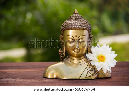 Golden buddha and  white aster flower. Chinese buddha sculpture and white dahlia flower on natural blur green background. Copy space
