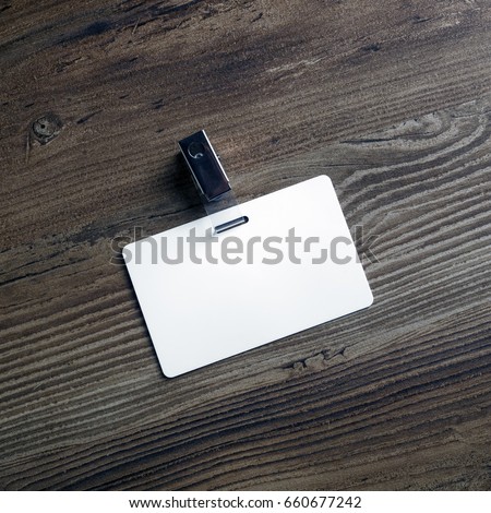 Photo of blank white plastic badge on wood table background. Blank id card. Template for your design. Top view.