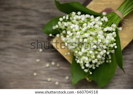 A bouquet of lilies of the valley on the background of an old book on a wooden table. Selective soft focus, blurred background