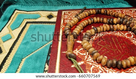 Rosary beads and al-quran on praying mat. Selective focus image. Contai arabic word meaning 'Al-Quran Al-Kareem'