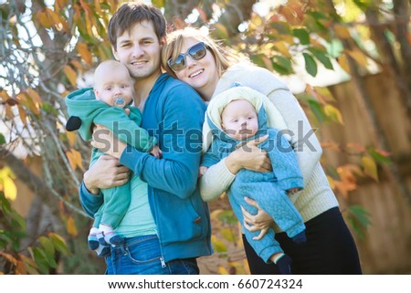 outdoor portrait of young happy smiling mother and father with twin babies on natural background