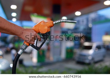 Hands holding a fuel nozzle on cars and blurred image of gas station with car refueling at night background.