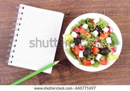 Fresh greek salad with vegetables and notepad for notes, concept of healthy nutrition, lifestyle and slimming