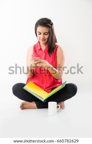 Pretty Indian/Asian young Girl using Cel/Smart Phone while studying, against white background