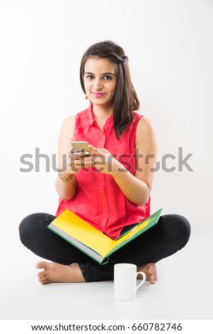 Pretty Indian/Asian College Girl studying from book and using Smartphone while sitting over white background