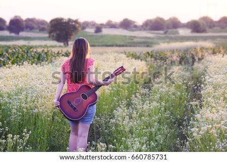 Woman with guitar in wild flowers field. Girl with a guitar on meadow in sunset