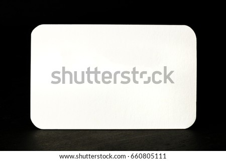 A photo of a blank white business card with rounded edges on a black texture. A mockup or a minimalist banner with copyspace