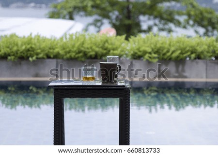 Whiskey and Irish Coffee on wooden small table with tropical swimming pool background. Tropical and rainy climate.