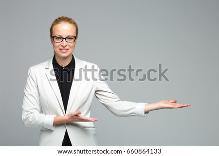 Beautiful young businesswoman wearing white attire and black eyeglasses, smiling, holding open palm with empty copy space. Business woman showing hand sign to side. Concept of advertisement product.