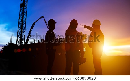 SilhouetteTeams Businessman engineer looking blueprint in a building site over Blurred construction site at sunset Royalty-Free Stock Photo #660890023