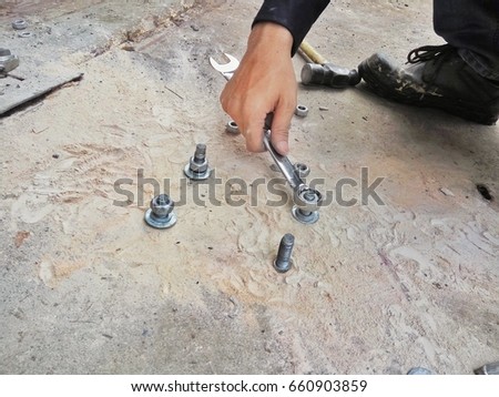 close up picture of man use wrench to install anchor bolt and fixing plate on the cement floor