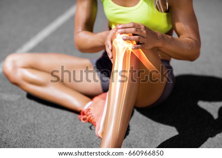 Low section of sportswoman suffering from knee pain while sitting on track during sunny day Royalty-Free Stock Photo #660966850