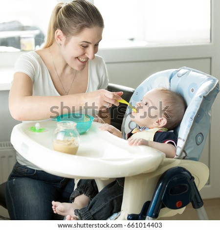 Beautiful smiling mother feeding her baby on kitchen